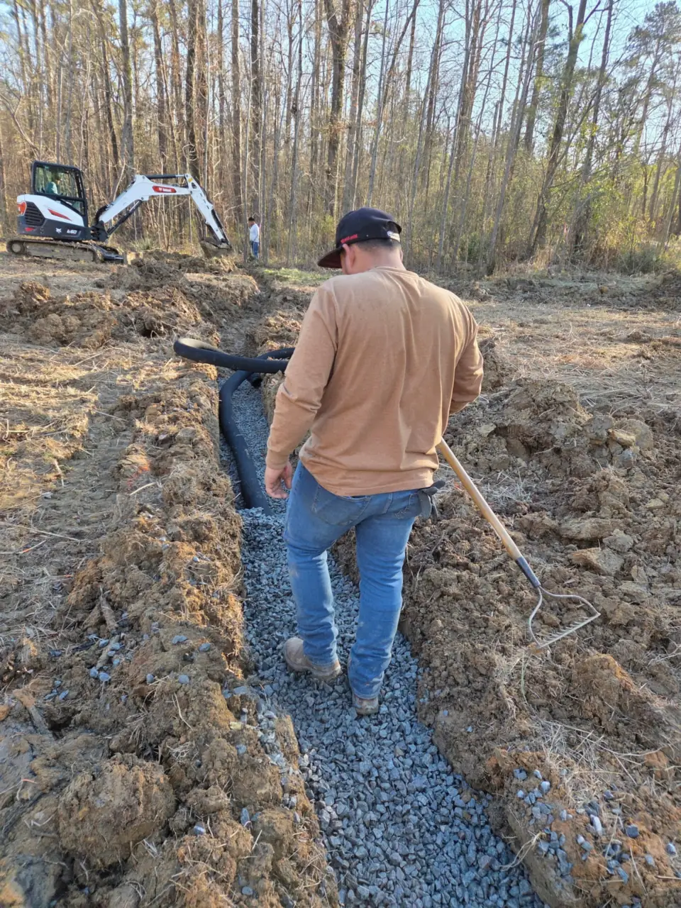 Crew member walking a gravel-filled French drain trench on a Columbia job site