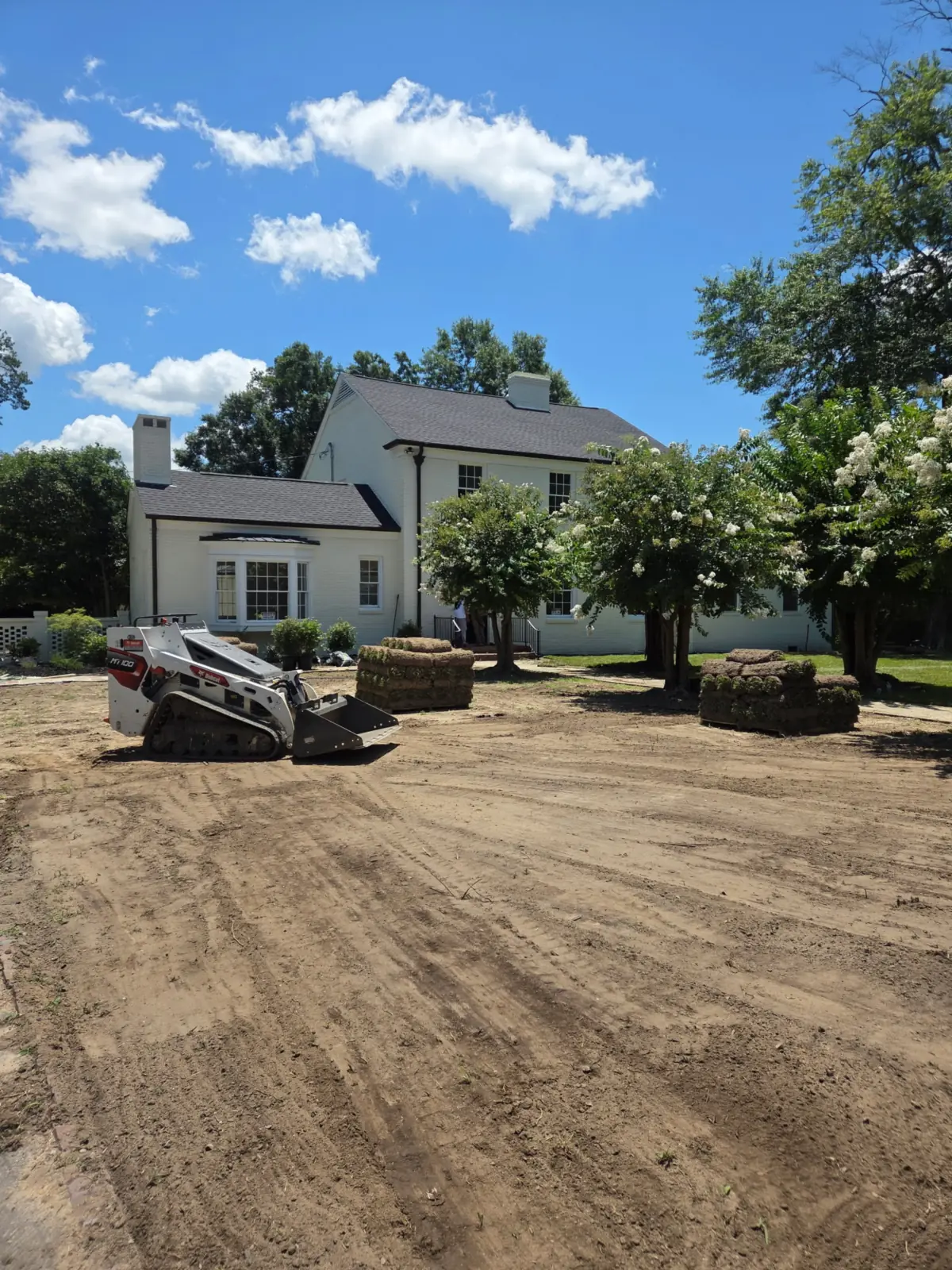 Skid steer grading bare soil with sod pallets staged for installation