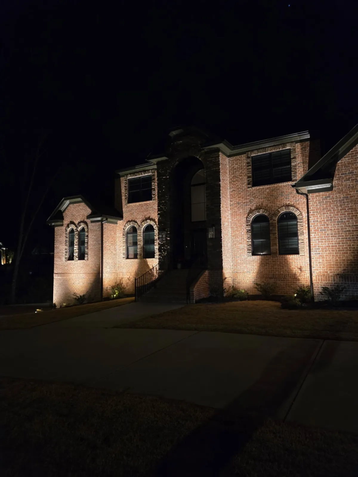 Brick home at night with landscape uplighting across the front