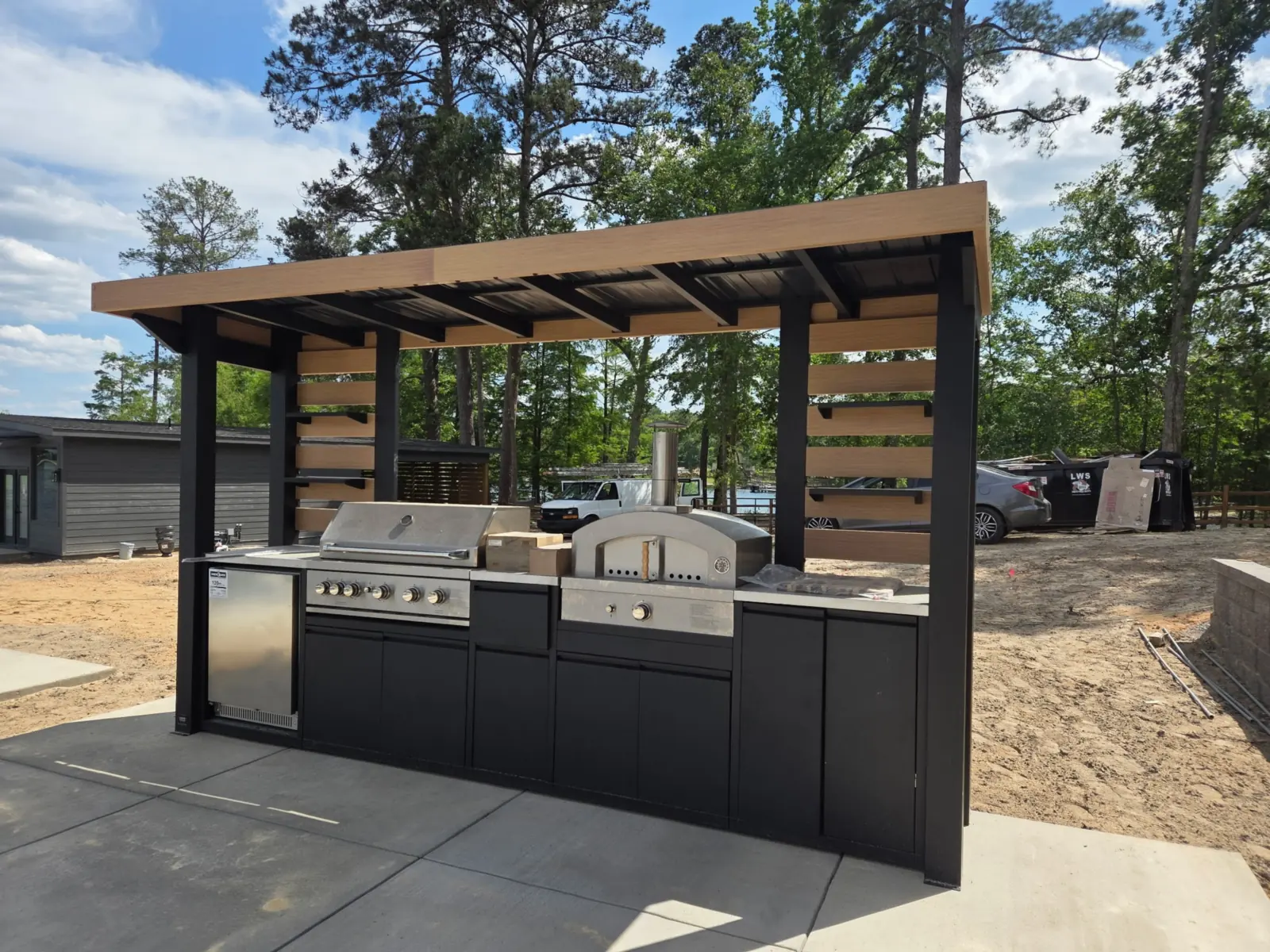 Outdoor kitchen with grill, pizza oven, and pergola on a new patio