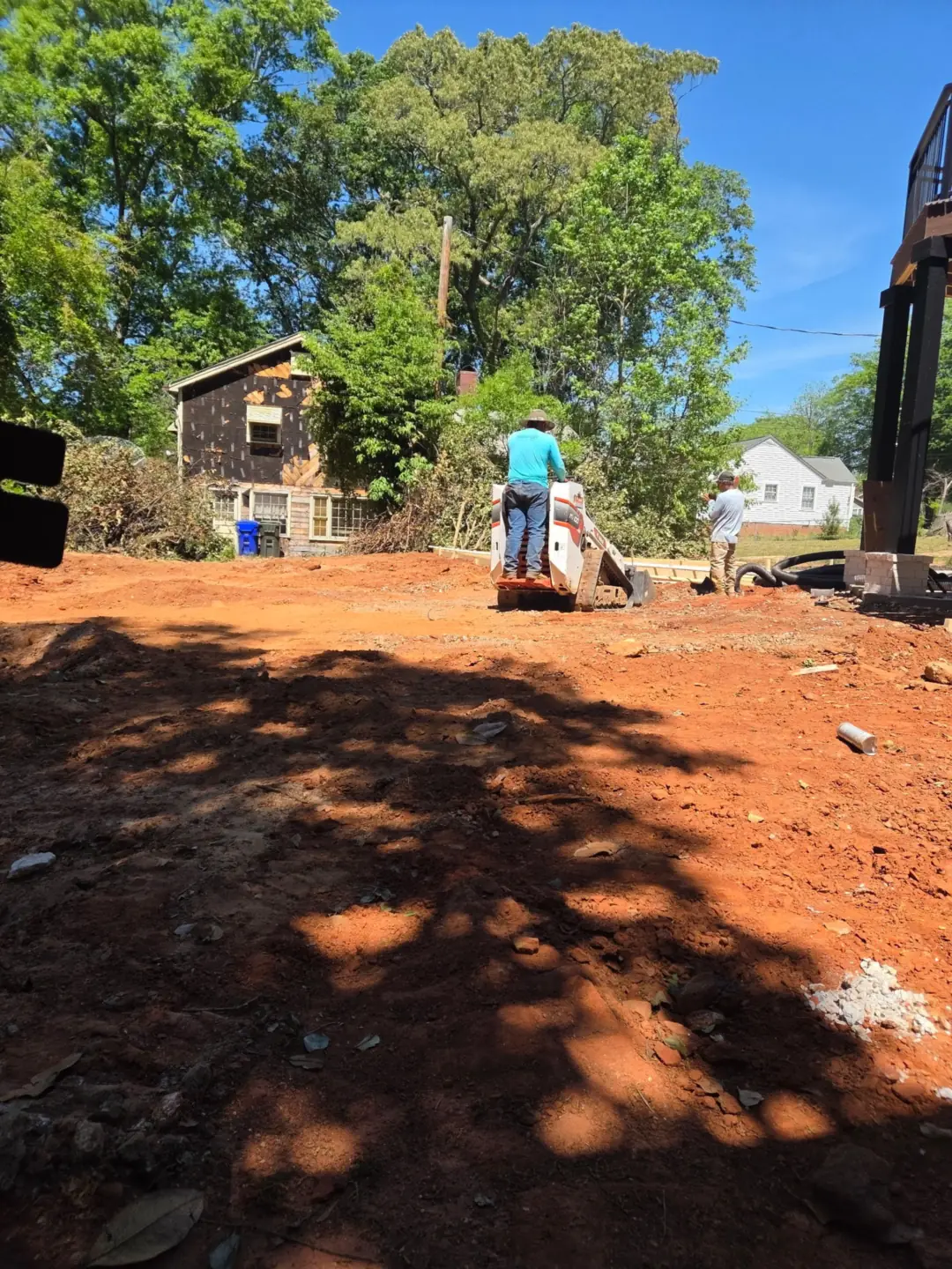 Crew grading red clay soil to prepare a yard for new landscaping